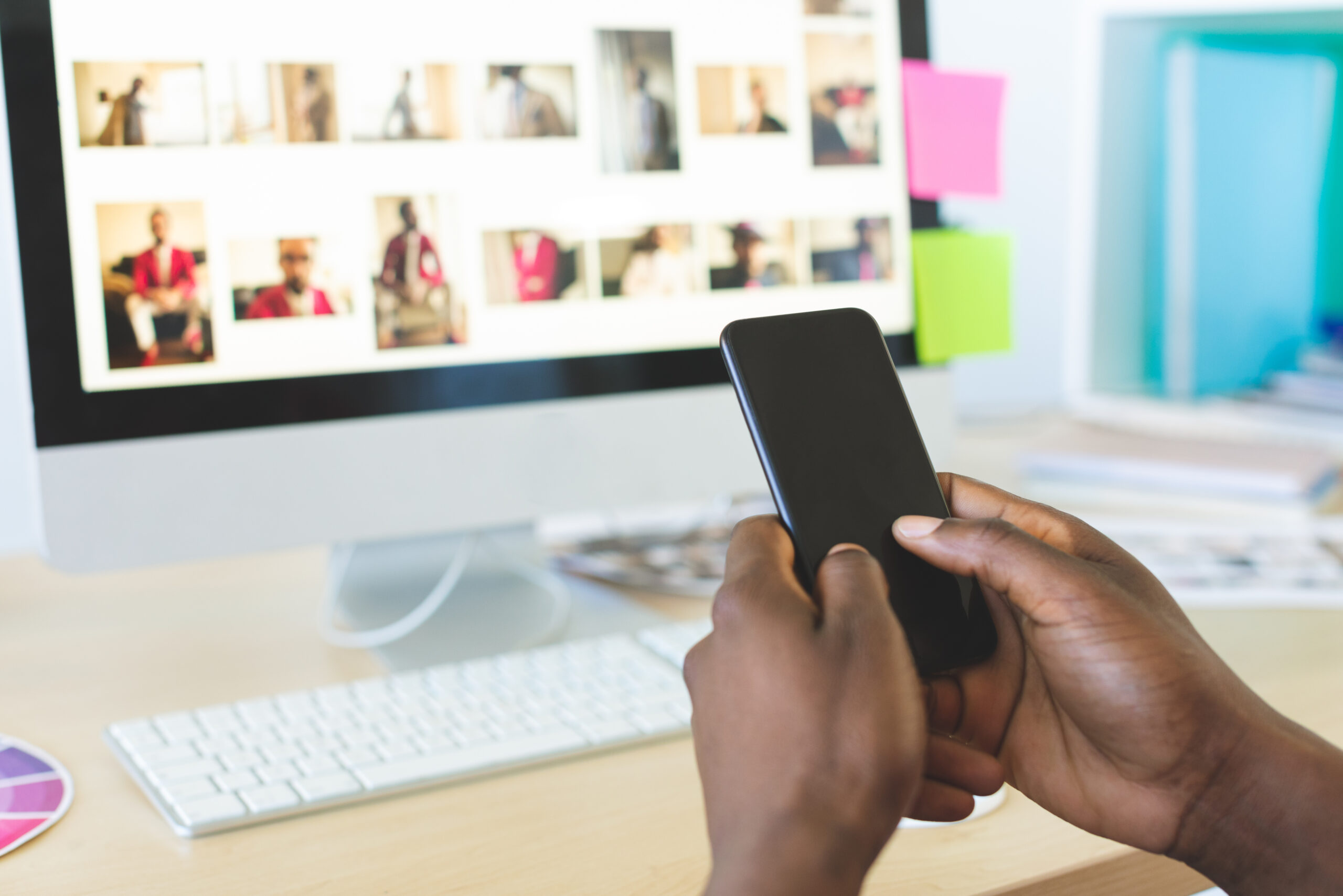 Rear view of young African-American graphic designer using mobile phone at desk in office